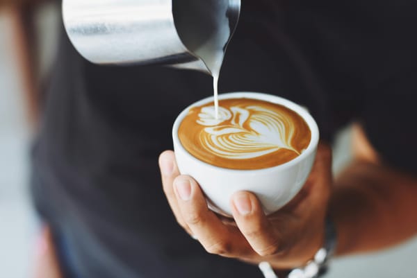 Person pouring milk into latte while holding cup in hand